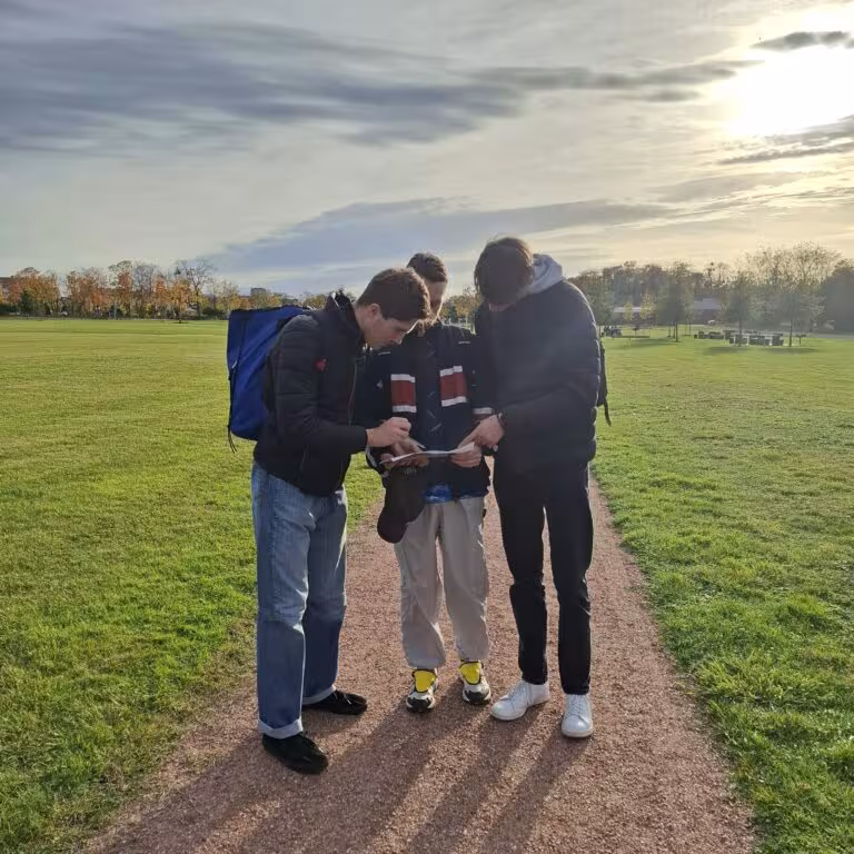 Trois jeunes personnes regardant un document dans un parc.